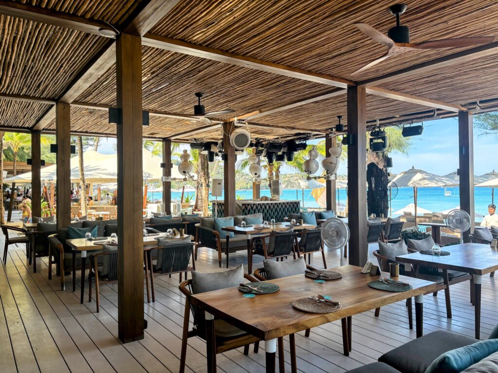 The open-sided dining terrace at Catch Beach Club, Bang Tao, Phuket, with wooden tables, rattan ceiling and views over turquoise sea