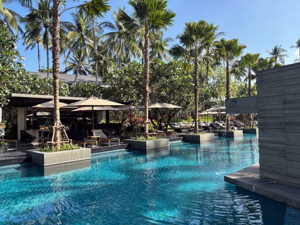 The lagoon pool at Twinpalms Surin, Phuket, with sun loungers, parasols and palm trees reflected in turquoise water