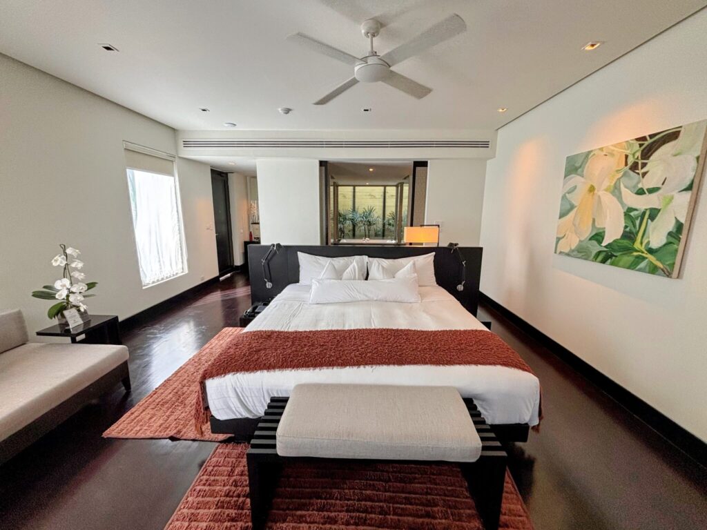 A lagoon suite at Twinpalms Surin, Phuket, with a super-king bed, dark wood floors, ceiling fan and floral artwork on the wall