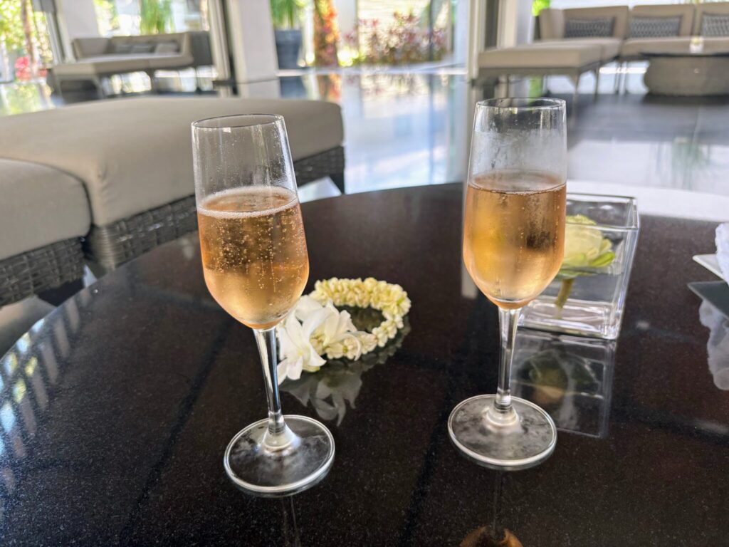 Two champagne welcome drinks and a jasmine phuang malai garland on a dark table at Twinpalms Surin, Phuket